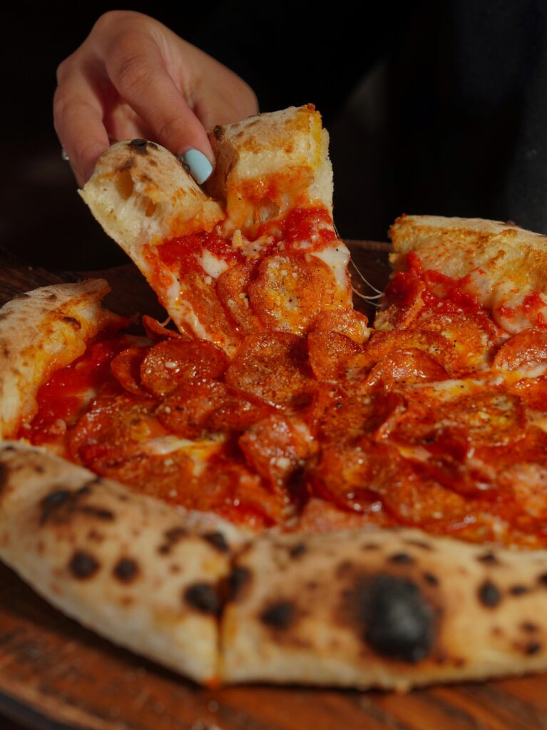 Delicious pepperoni pizza slice being lifted from a wood-fired pie with melted cheese.