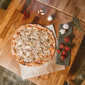 Top-down view of a homemade mushroom pizza surrounded by fresh ingredients on a wooden table.